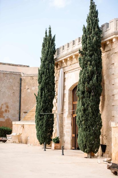 Two tall cyprus trees next to the old wooden fortress drawbridge entrance at cap rocat wedding venue in mallorca