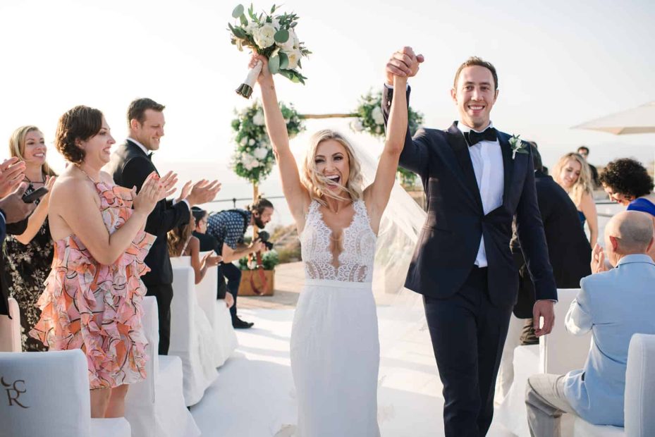 just married couple celebrate coming back up the aisle with arms in the air at cap rocat wedding venue in mallorca spain
