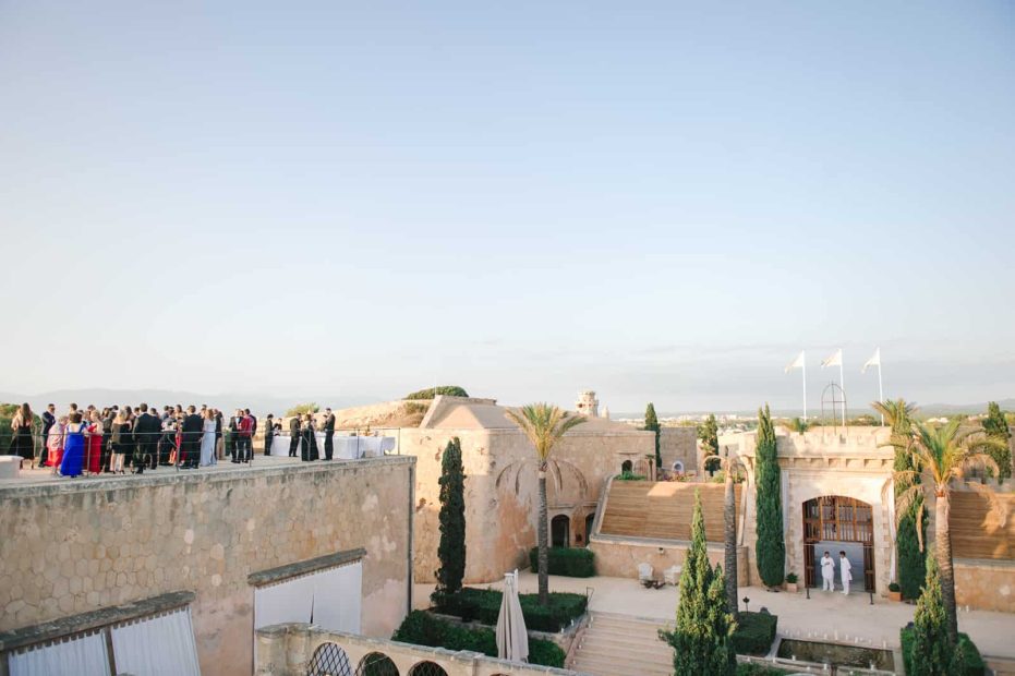 wedding guests ready for the wedding ceremony at old fortress wedding venue cap rocat with 3 white flags and Cyprus trees inn the background