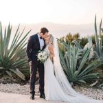 Bride and Groom Kat and Alex kiss near large, wild aloe vera plant with the sea in the background at Cap Rocat Wedding venue in Mallorca