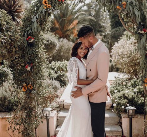 the groom kissing the brides head under a floral archway at their wedding at spanish wedding venue casa la siesta