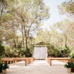 outdoor ceremony set up with wooden benches and a floral square backdrop amongst the trees at ibiza wedding venue ca na xica