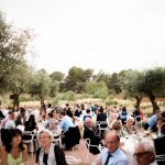 wedding guests dine at round tables surrounded by olive trees on the grounds of wedding venue ca na xica in ibiza spain