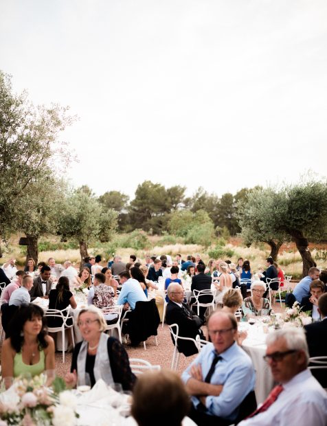 wedding guests dine at round tables surrounded by olive trees on the grounds of wedding venue ca na xica in ibiza spain