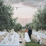 bride and groom walking between tables in olive grove at wedding venue in puglia masseria don luigi