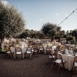 wedding breakfast tables set up ready for guests between olive trees and underneath fair lights at wedding venue ca na xica in ibiza