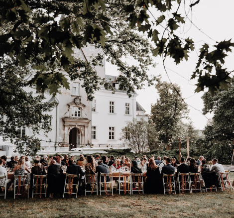 wedding guests sat down at wooden tables for al fresco wedding reception of polish wedding venue the palace osowa sien