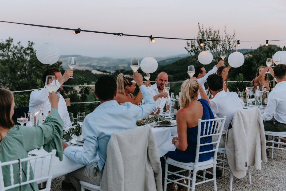 wedding guests raising a glass to the bride and groom whilst dining al fresco at Italian wedding venue at sunset