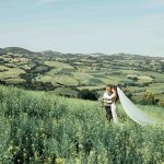 bride sat in grooms arms whilst in a field surrounding Italian wedding venue le stonghe