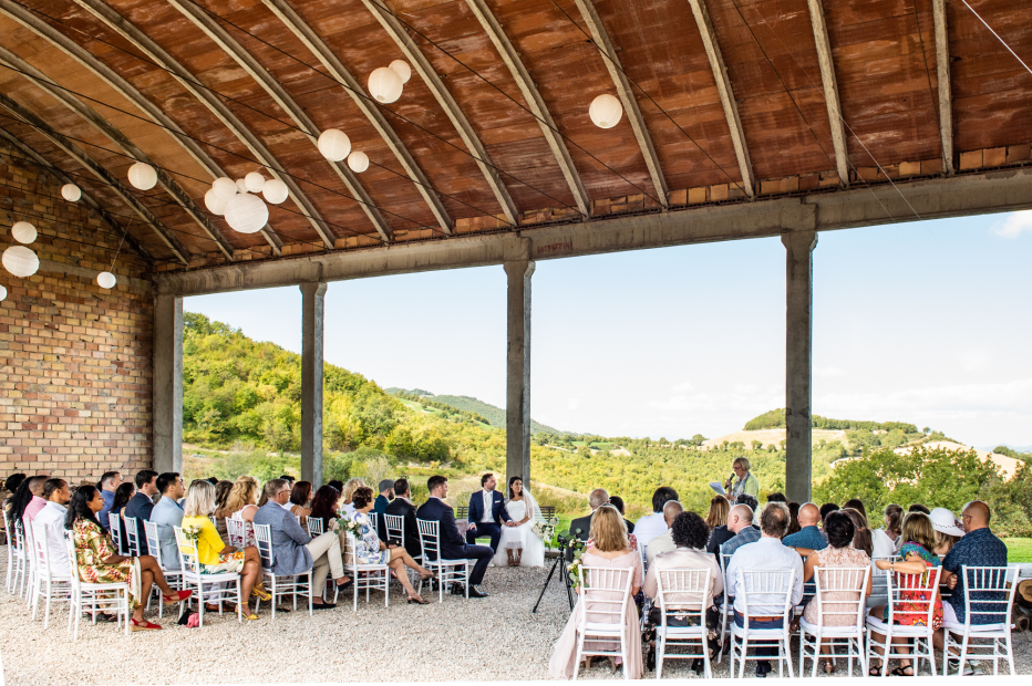 gran overhead barn style building with 100 wedding guests seated for wedding ceremony in Italy