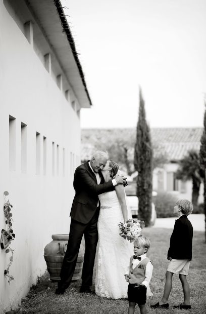 black and white photo of bride and groom kissing stood beside their children