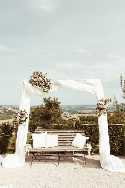 Ceremony archway with draped white chiffon fabric and flowers at Italian wedding venue