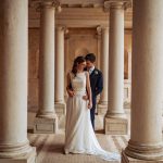 bride and groom stood together between the columns of the exterior at Italian wedding venue Villa Imperiale Pesaro