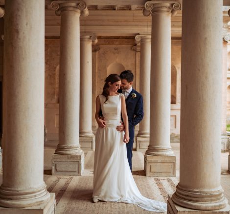 bride and groom stood together between the columns of the exterior at Italian wedding venue Villa Imperiale Pesaro