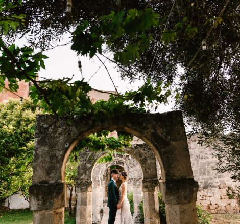 bride and groom underneath the unique stone archway on the grounds of Italian wedding venue masseria spina