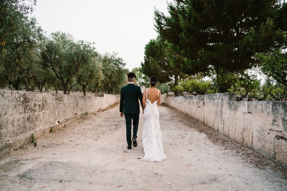ride and groom walking down the stone driveway between rows of olive groves at Italian wedding venue masseria spina