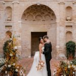 bride and groom stood together in front of beautiful old stone archway at Villa Imperiale in Italy