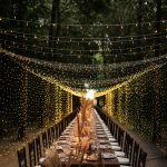 view down the centre of a long wedding table amongst the forest with overhead fairy lights at convent dell'Annunciata in Italy