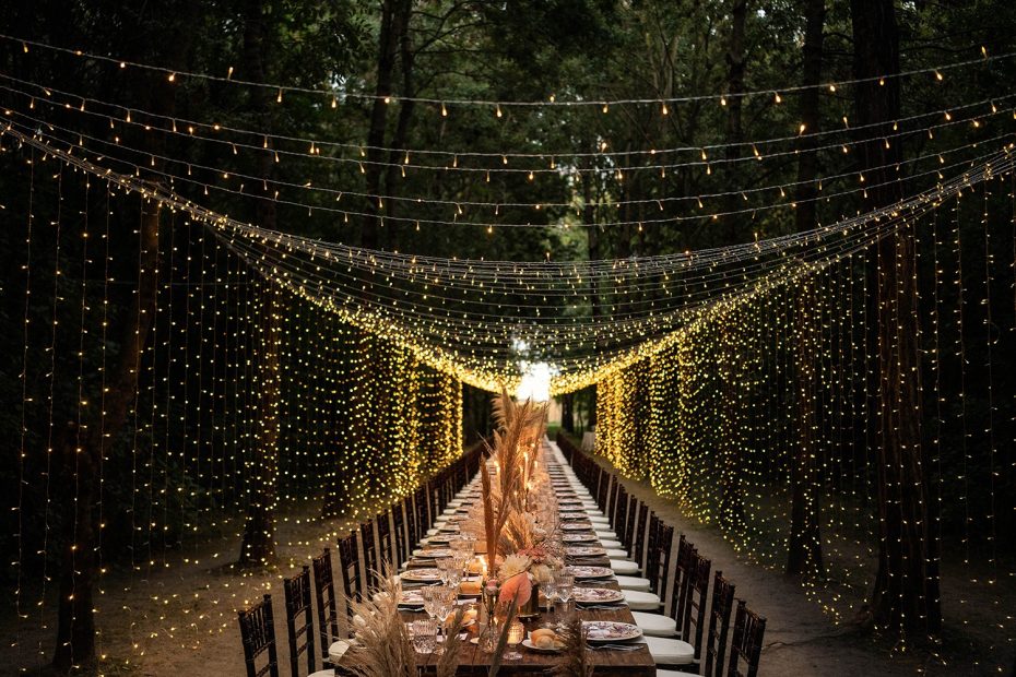 view down the centre of a long wedding table amongst the forest with overhead fairy lights at convent dell'Annunciata in Italy