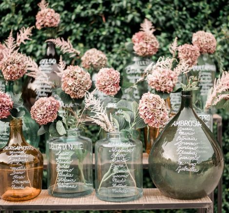 table names written in white ink on different glass vases at Italian wedding venue