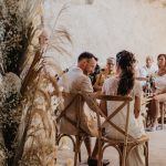 view from behind bride and groom as they sit at the aisle making their vows on wooden chairs at le Petit Roulet wedding venue in luberon in france