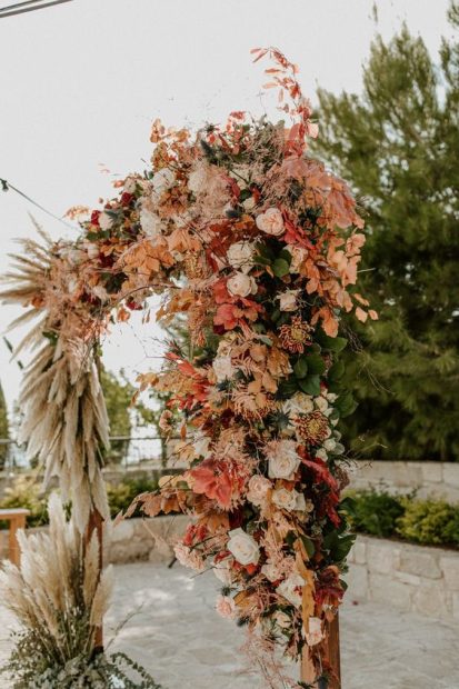 flowers and pampas grass in pinks and neutral tones over wooden square ceremony aisle arch at wedding venue in Cyprus liopetro