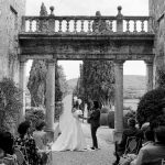 black and white photo of bride and groom under stone arch at wedding venue in Tuscany Italy Borgo Stomennano