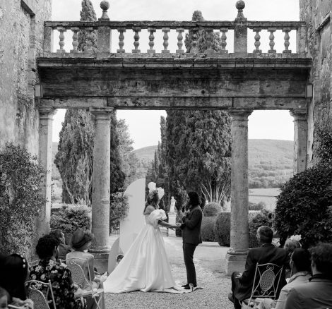 black and white photo of bride and groom under stone arch at wedding venue in Tuscany Italy Borgo Stomennano
