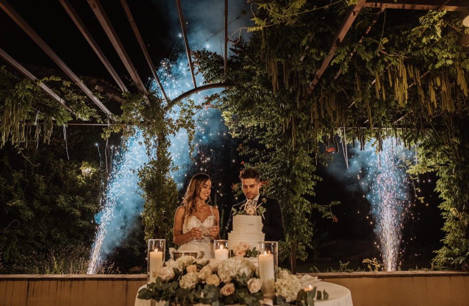 bride and groom with fireworks in the background cutting the cake at wedding venue in italy