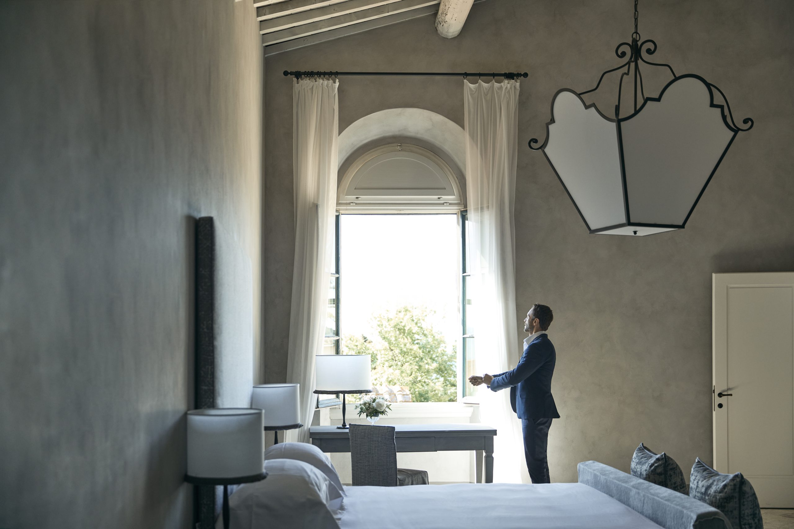 Groom getting ready by window in bridal suite at luxury wedding venue in Tuscany COMO Castello Del Nero
