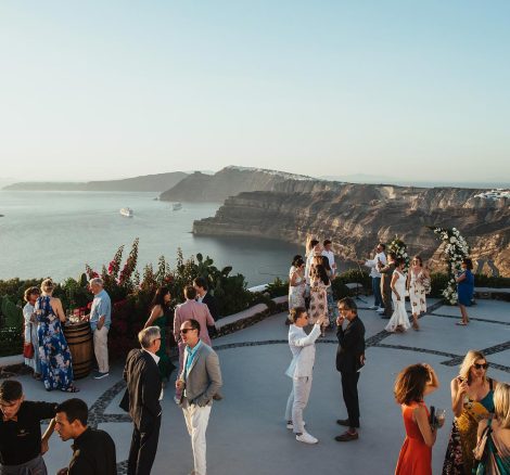 wedding guests mingling on cliff edge during reception drinks at wedding venue in Santorini venetsanos winery
