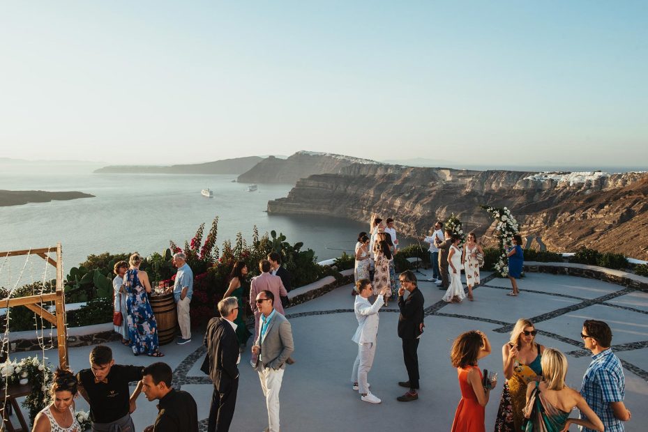 wedding guests mingling on cliff edge during reception drinks at wedding venue in Santorini venetsanos winery