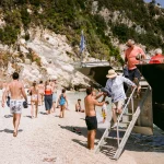 Image of wedding guests leaving a boat on a beach at wedding venue The Peligoni Club