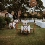 wedding tables and hanging rattan lampshades oustide wooden benches and pampas for wedding ceremony outside at wedding venue in france provence