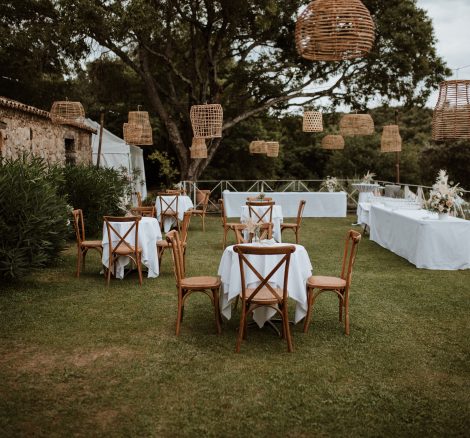 wedding tables and hanging rattan lampshades oustide wooden benches and pampas for wedding ceremony outside at wedding venue in france provence