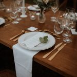close up of crockery set up with gold cutlery and wooden tables at wedding venue in france provence