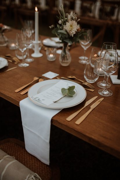 close up of crockery set up with gold cutlery and wooden tables at wedding venue in france provence