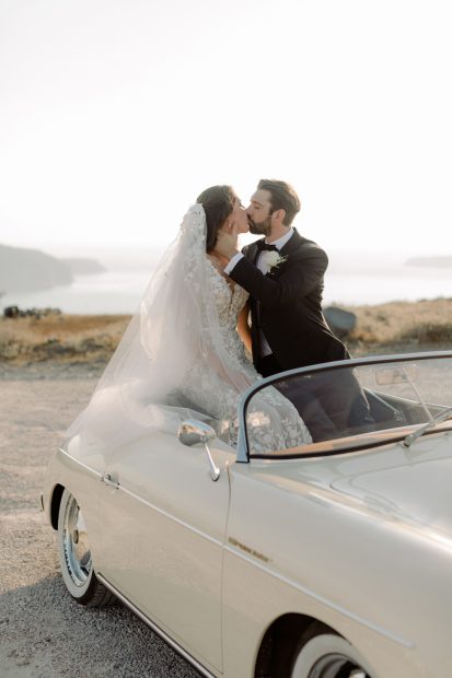 classy bride and groom sit in open top vintage car at wedding venue in Santorini venetsanos winery