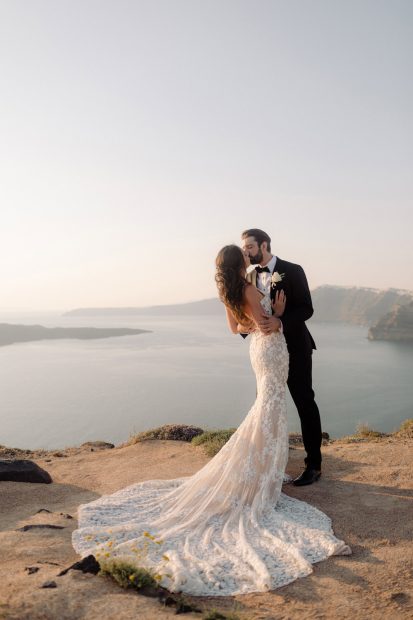 bride and groom kissing o the cliff edge at wedding venue in Santorini venetsanos winery