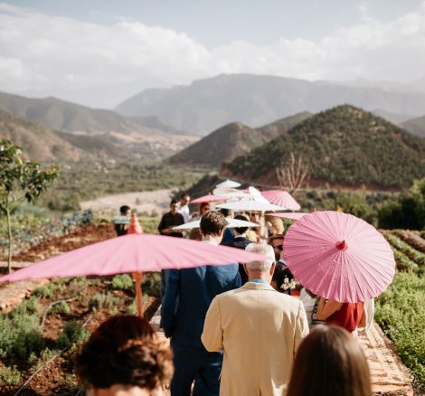 wedding guests walk to the outdoor wedding ceremony with colourful parasols at unique wedding venue in morocco kasbah bab ourika