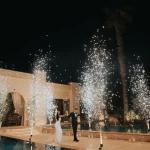Image of married couple walking with fireworks by pool at wedding venue Ktima Orizontes, Athens, Greece