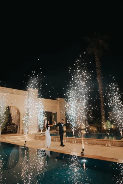 Image of married couple walking with fireworks by pool at wedding venue Ktima Orizontes, Athens, Greece