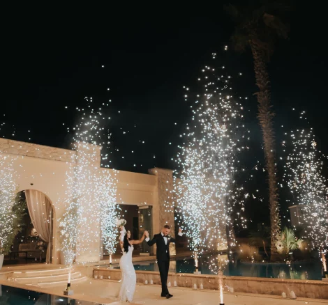 Image of married couple walking with fireworks by pool at wedding venue Ktima Orizontes, Athens, Greece