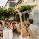 Image of married couple entering room with guests at dinner tables at wedding venue Domaine du Rodier