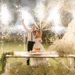 Image of couple with fireworks behind them as they cut their cake at wedding venue Masseria Alchimia