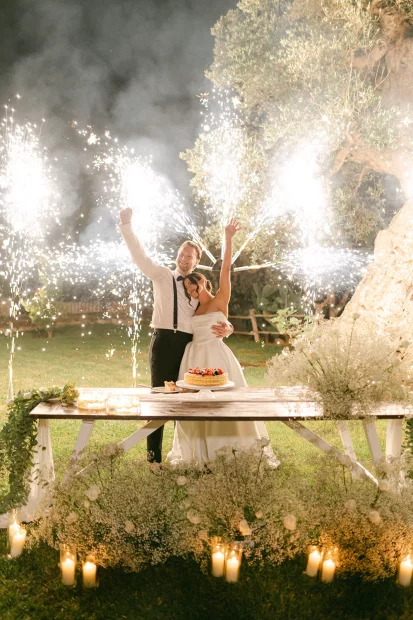 Image of couple with fireworks behind them as they cut their cake at wedding venue Masseria Alchimia
