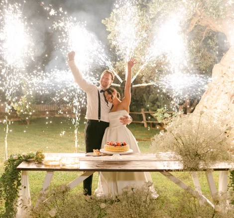Image of couple with fireworks behind them as they cut their cake at wedding venue Masseria Alchimia