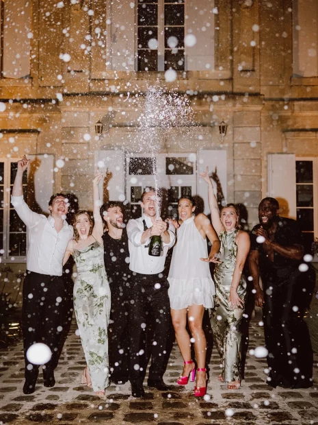 Image of group of people spraying champagne at wedding venue Château de Garde, France