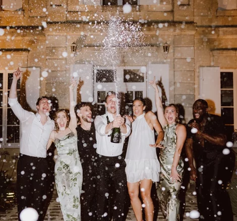 Image of group of people spraying champagne at wedding venue Château de Garde, France
